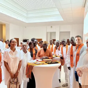 Groupe de personnes en tenue blanche avec des écharpes orange autour d'une table.