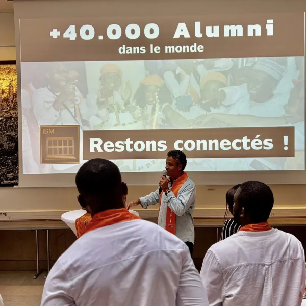 Photographie d'un homme donnant une présentation, public vêtu de blanc.